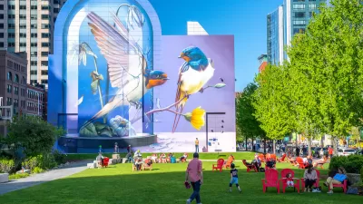 People enjoying a sunny day on a green lawn with pink lawn chairs and colorful bird mural in background in Boston, Massachusetts.