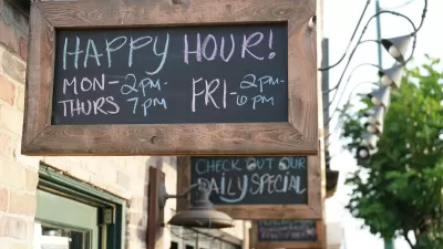 Close-up of rustic wood-framed chalkboard sign with happy hours listed above green restaurant doorframe on small commercial street.