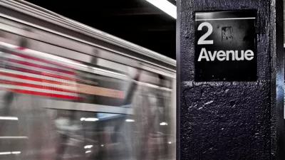 Close-up of 2 Avenue sign on column in NYC subway station with train passing by in background.