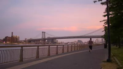 Sunset view of Williamsburg Bridge from East River Park walkway next to river with one jogger.