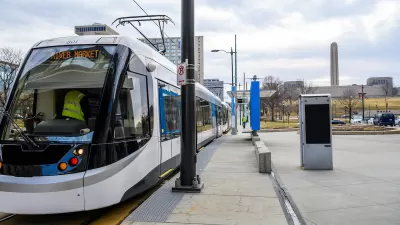 White and blue Kansas City streetcar at a station with LIberty Memorial column in background.
