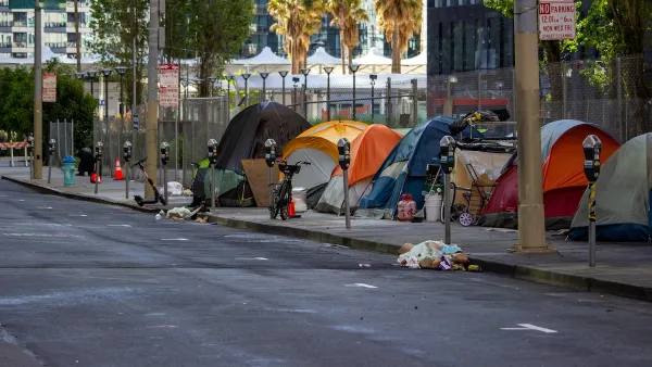 Line of tents set up against a fence on a public sidewalk in San Francisco, California with bikes and personal items around.