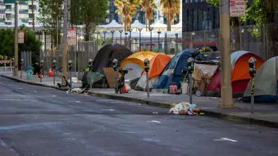 Line of tents set up against a fence on a public sidewalk in San Francisco, California with bikes and personal items around.