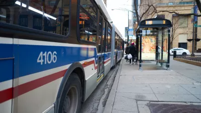 White, blue, and red Chicago transit bus at an urban bus station with shelter.