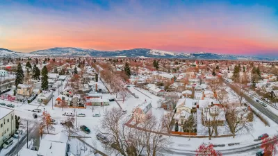 Large homes in neighborhood covered in snow in Missoula, Montana with mountains in background gainst sunset sky.