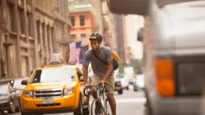 Sepia-toned photo of man riding bicycle on urban street with yellow cab and historic brick buildings in background.