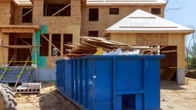 Large blue metal dumpster container in front of wood-frame house under construction.
