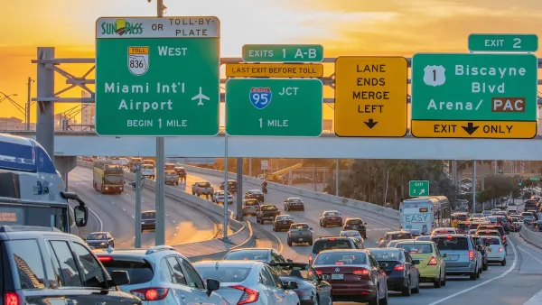Traffic on Miami freeway with signs for Miami airport and other exits at sunset.