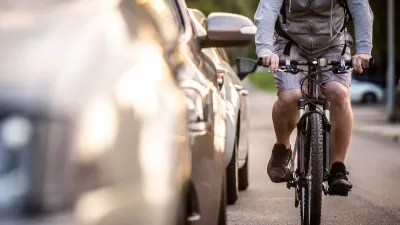Man on bike rides next to parked cars.