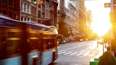 Blurred image of New York City bus driving through intersection with 5th Avenue with golden hour sunset sky in background.
