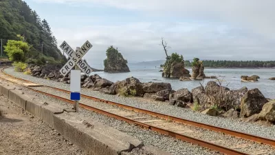 Railroad crossing sign next to tracks along rocky coast in Oregon.
