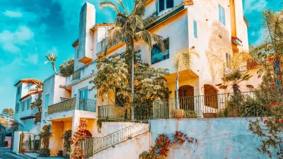 Line of white stucco, multistory luxury homes on street.