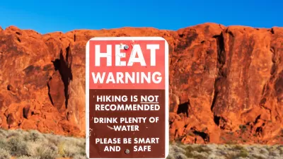 Extreme heat warning sign outdoors with red desert rock cliff in background.