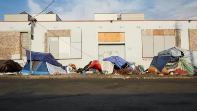 Small tents set up on sidewalk by unhoused people next to boarded-up one-story industrial building in San Francisco, California.