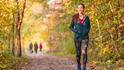 Woman in leggings and long-sleeved jacket walks in public park among fall foliage