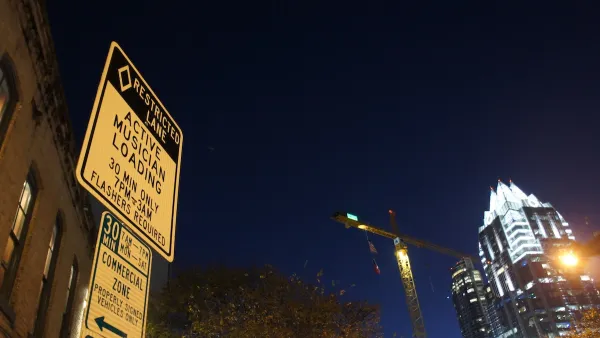 Close-up of musicians loading zone sign on Sixth Street in Austin, Texas at night with illuminated high-rise with pyramidal top in background.