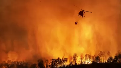 Firefighting helicopter sillhouetted against orange nighttime wildfire in California with trees visible at bottom of image.