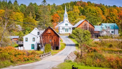 Rural community qith quaint homes and white steepled church against forest with fall colors and German shepherd dog in foreground.