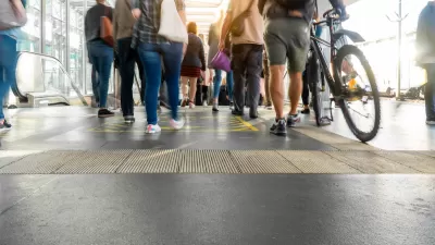 Walkways and escalator at crowded transit station, with one person walking a bike in foreground.