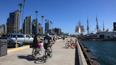 People biking along beach path with moored ship in San Diego, California.