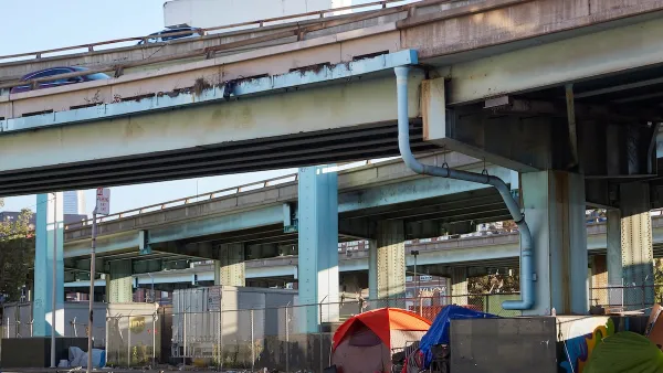 Tents set up against fence by unhoused people under freeway overpass in San Francisco, California.