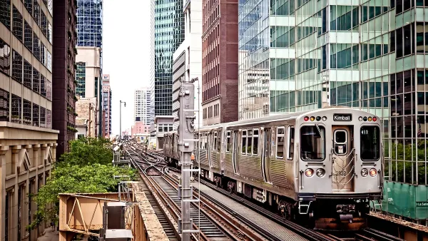 Silver Chicago train passing by dense high-rise buildings on elevated track.