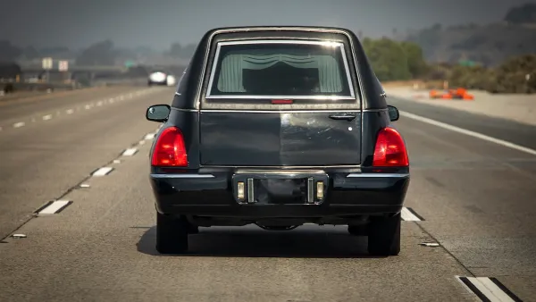 Black hearse seen from behind driving on multilane road.