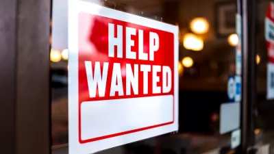 Close-up of Help Wanted sign with white text on red background posted inside storefront window.
