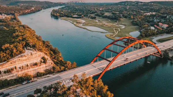 Aerial view of Pennybacker Bridge in Austin, Texas. Bridge over river with orange arches and downtown Austin visible in far background.