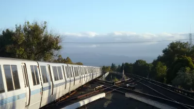 BART heavy rail train on elevated track pulling into Concord, CA station with cloudy sky and trees in background.