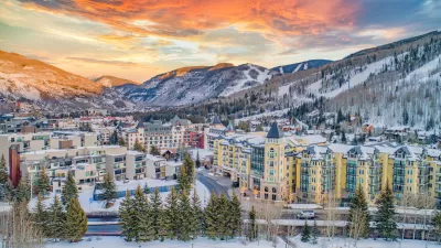 Aerial view of Vail, Colorado in winter with multi-story buildings in foregorund and snowy mountains in background.