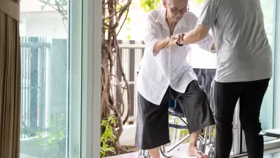 Elderly woman enters house with help from caregiver who is holding her hands