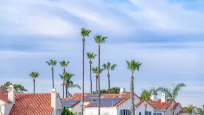 View of red tiled rooftops with solar panels and tall palm trees between houses