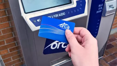 Close-up of person's hand holding blue ORCA transit fare payment card in front of fare payment machine.