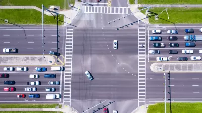 Bird-s eye view of multi-lane road intersection with medians and crosswalks.