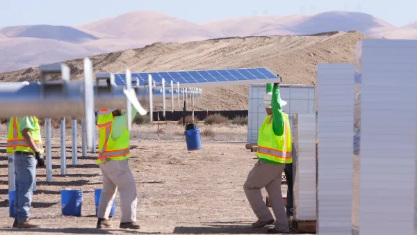 Workers in safety vests installing large solar panels in Southern California desert landscape.