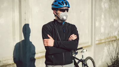 Male cyclists wearing helmet, sunglasses, and N95 mask stands with arms crossed in front of his bike