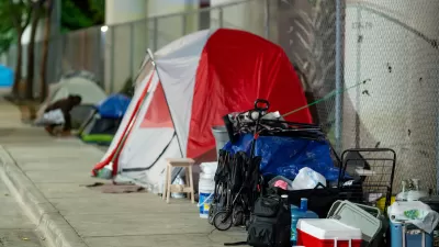 A red and white tent on the sidewalk with other belongings of an unhoused resident in Miami, Florida.