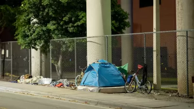 Tent occupied by unhoused resident with bike against fence under underpass in Miami, Florida.
