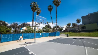 Concrete basketball court with clear glass backboard and palm trees in background in Los Angeles, California.