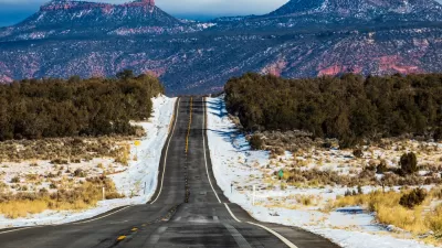 Asphalt road with Bears Ears National Monument rock formations in background.