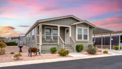 Front of pale green manufactured home with carport and desert sunset in background.