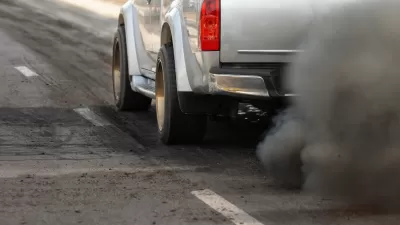Close-up of driver's side of silver truck with cloud of dirty emissions from tailpipe.