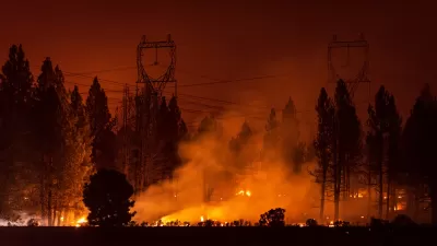 Wildfire burning under power transmission towers and large trees at night.