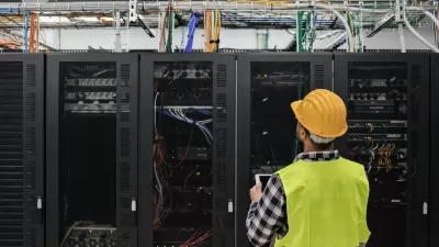 Worker in yellow safety vest and hard hat looks up at servers in data center.
