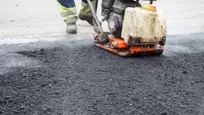 Close-up of worker using machine to press down fresh asphalt on road.