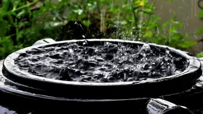 Close-up of top of black rain barrel full of water with raindrops falling on surface.
