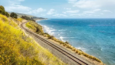 Train tracks along California coast with yellow wildflowers blooming on one side and blue Pacific Ocean on the other.