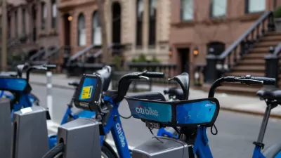 Blue Citi Bike bicycles parked at a station in New York City with blurred brick brownstones in background.