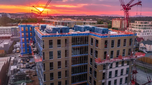 Multistory building under construction with large crane against sunset sky.